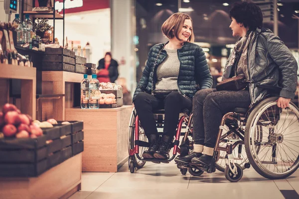 Dos mujeres con discapacidad sonrientes en silla de ruedas en una tienda departamental — Foto de Stock