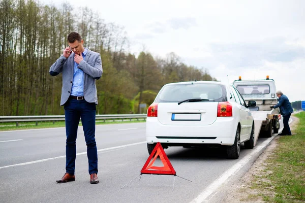 Homem chamando enquanto reboque caminhão pegando seu carro quebrado — Fotografia de Stock