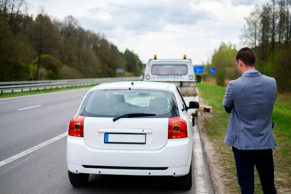 Homem chamando enquanto reboque caminhão pegando seu carro quebrado — Fotografia de Stock