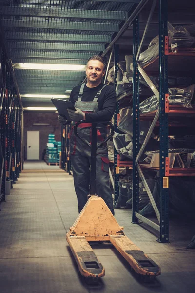 Storekeeper trabalhando com caminhão de paletes em um armazém — Fotografia de Stock