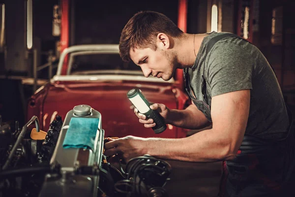 Механик, работающий над классическим автомобильным двигателем в мастерской — стоковое фото