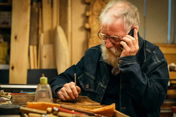 Senior hout snijwerk professionele met mobiele telefoon — Stockfoto