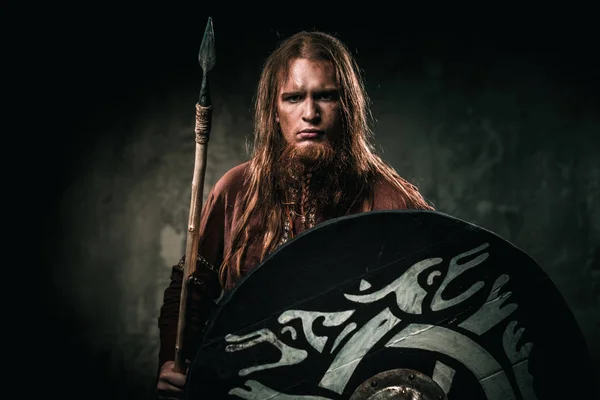 Ernstige viking met een speer in de kleren van een traditionele warrior op een donkere achtergrond. — Stockfoto