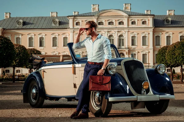 Уверенный в себе богатый молодой человек с портфелем рядом с классическим кабриолетом — стоковое фото