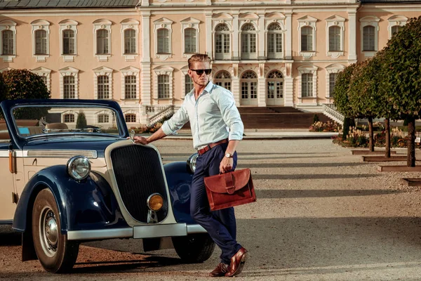 Selbstbewusster, wohlhabender junger Mann mit Aktentasche in der Nähe klassischer Cabrios — Stockfoto