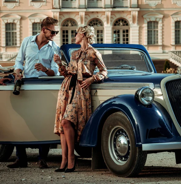 Богатая пара рядом с классическим кабриолетом против королевского дворца — стоковое фото