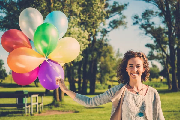 Gelukkig meisje met regenboog-gekleurde lucht ballonnen in een park. — Stockfoto