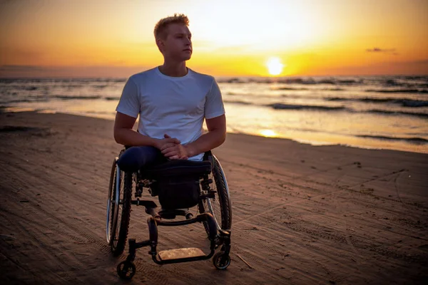 Handicapped man in wheelchair and his girlfriend alone on a beach at sunset — 스톡 사진