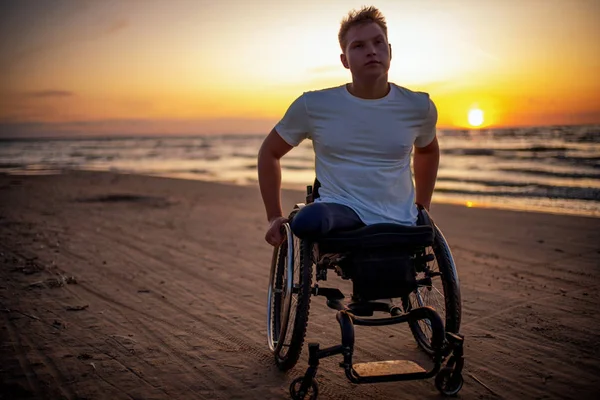 Gehandicapte man in rolstoel en zijn vriendin alleen op een strand bij zonsondergang — Stockfoto