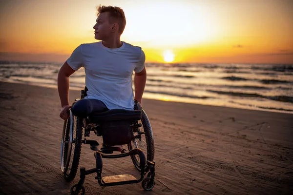 Handicapped man in wheelchair and his girlfriend alone on a beach at sunset — 스톡 사진