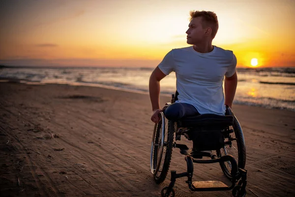 Gehandicapte man in rolstoel en zijn vriendin alleen op een strand bij zonsondergang — Stockfoto