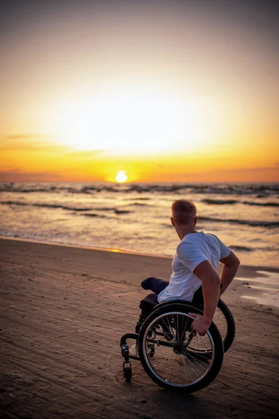 Gehandicapte man in rolstoel en zijn vriendin alleen op een strand bij zonsondergang — Stockfoto