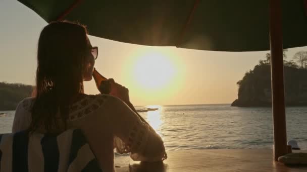 巴厘岛，一个女人日落时在海滩上喝啤酒 — 图库视频影像