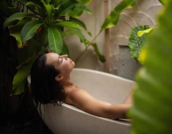 Femme relaxante dans un bain extérieur avec des feuilles tropicales à Bali — Photo