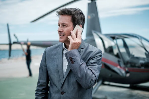 Бизнесмен разговаривает по телефону возле частного вертолета — стоковое фото