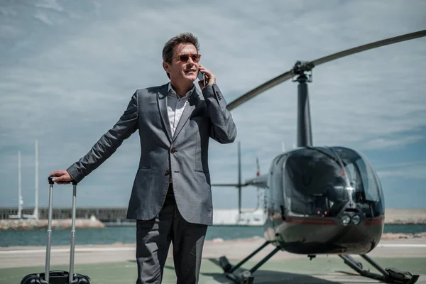 Бизнесмен разговаривает по телефону возле частного вертолета — стоковое фото
