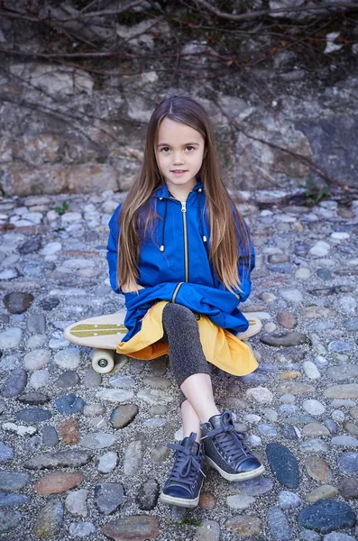 Niña positiva sentada en el monopatín —  Fotos de Stock