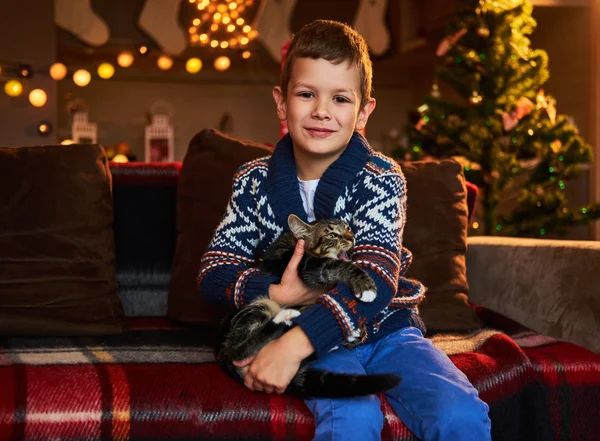Boy sits on a couch and holds cat — ストック写真