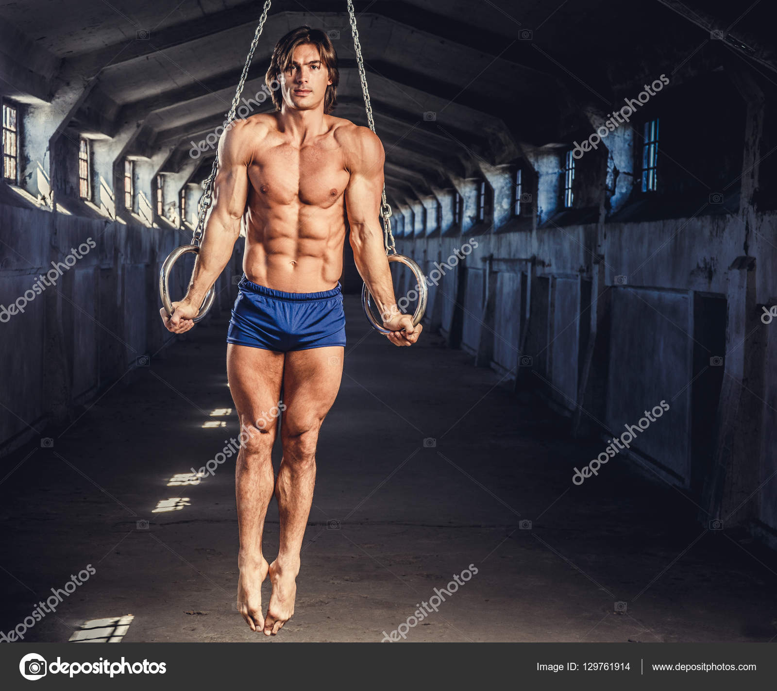 Athletic muscular male posing with gymnastic rings in a dark