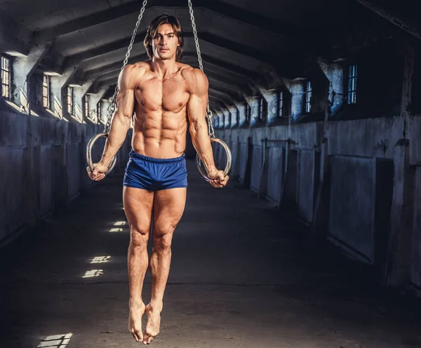 Hombre musculoso posando con anillos gimnásticos — Foto de Stock