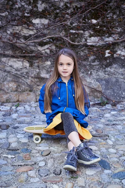 Niña positiva sentada en el monopatín —  Fotos de Stock