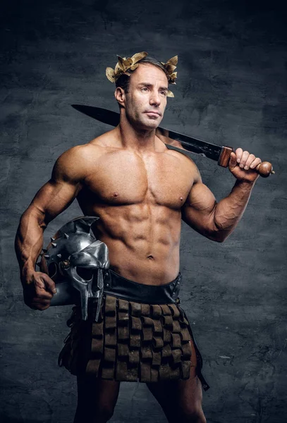 Muscular man holding helmet and sword — Stock Photo, Image