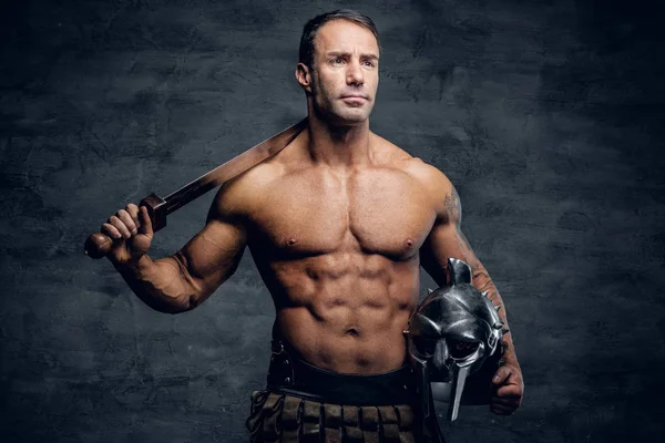 Muscular man holding helmet and sword — Stock Photo, Image