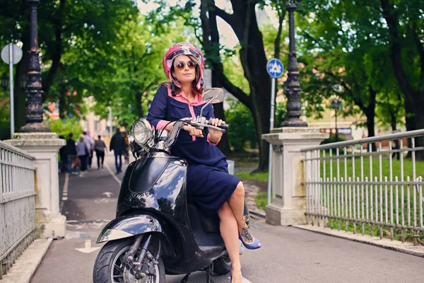 Vrouw in een jurk die zittend op een moto-scooter — Stockfoto