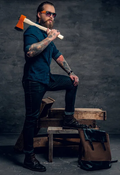 Tattooed man in sunglasses holding an axe. — Stock Photo, Image