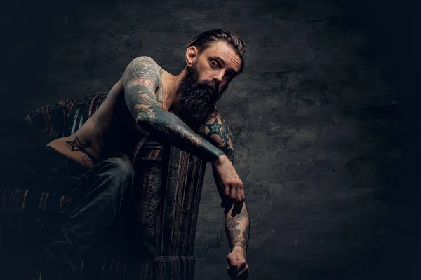 Shirtless, tattooed man sitting on a chair — Stock Photo, Image