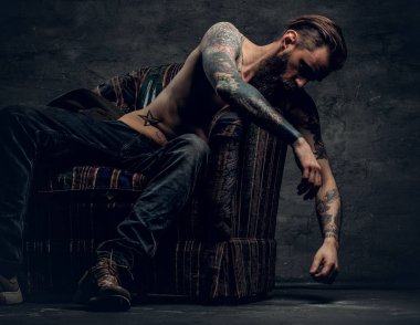 Gömleksiz, dövmeli adam bir sandalyede oturuyor