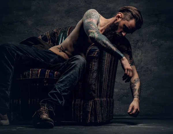Sem camisa, homem tatuado sentado em uma cadeira — Fotografia de Stock