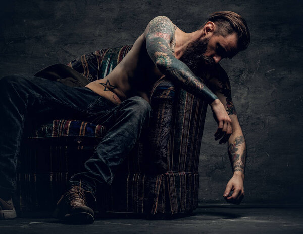 Мужчина без рубашки и татуировки сидит на стуле
