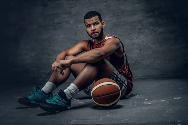 Jogador de basquete sentado em um chão com bola — Fotografia de Stock