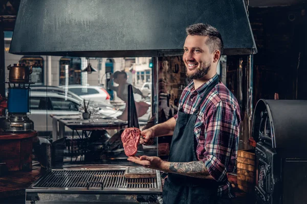Un beau chef barbu tient un steak de bœuf — Photo