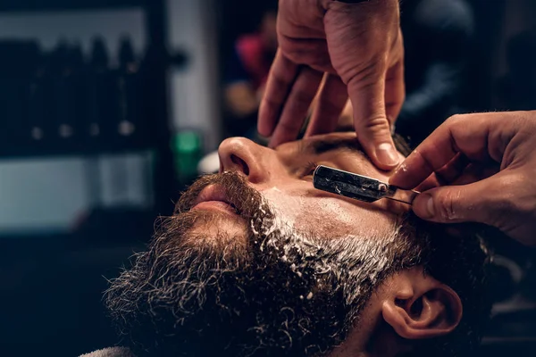 Barbeiro barbeando barba macho com uma navalha afiada — Fotografia de Stock