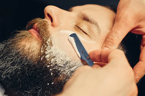 Barber shaving bearded male with a sharp razor — Stock Photo, Image