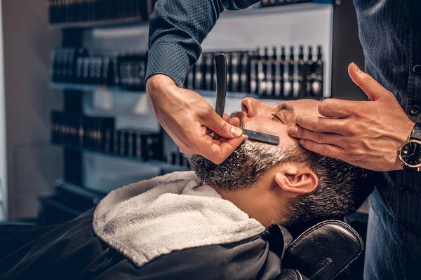 Парикмахер бреет бородатого мужчину острой бритвой — стоковое фото