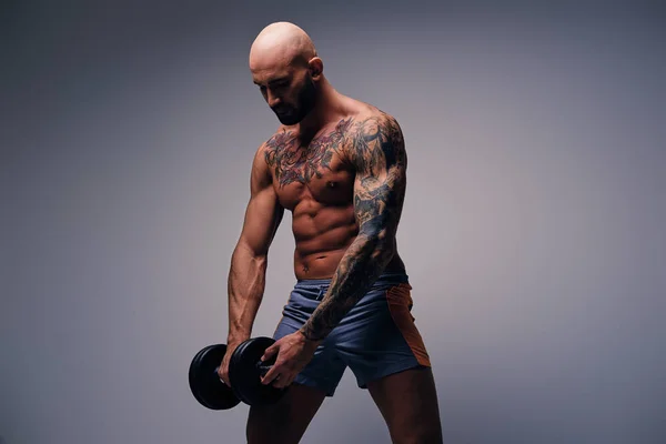 Athletic man with tattoos holds dumbbell — Stock Photo, Image