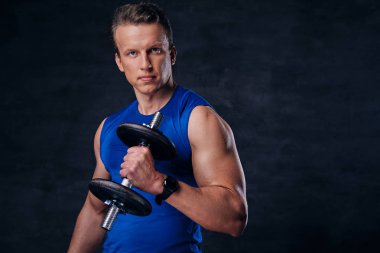 İçinde mavi bir spor giyim giyinmiş bir adam halter karanlık üzerinde tutar. 