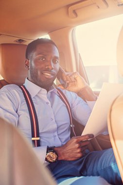 Blackman mavi gömlekli otomobilin arka koltukta oturur.