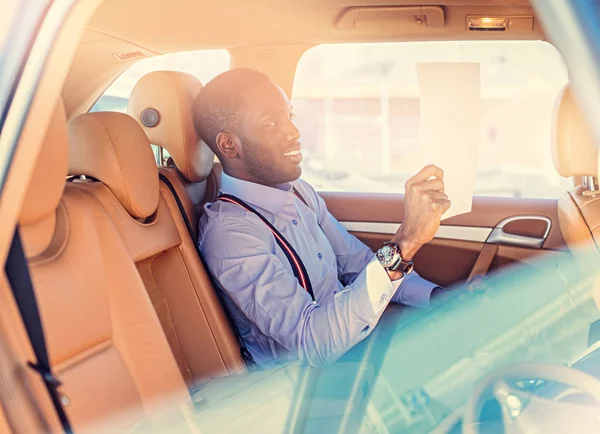 Blackman in a blue shirt sits on car's back seat. — Stock Photo, Image