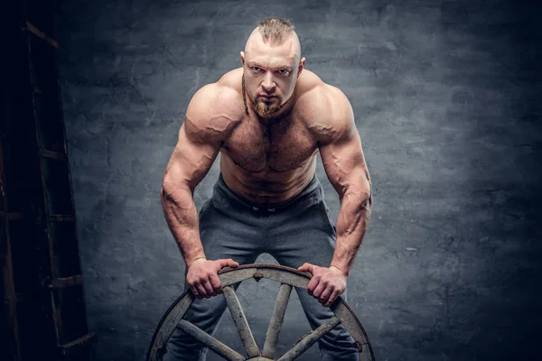 Hunk bodybuilder holds wooden wheel — Stock Photo, Image