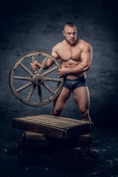 Bodybuilder houdt oude houten wiel — Stockfoto