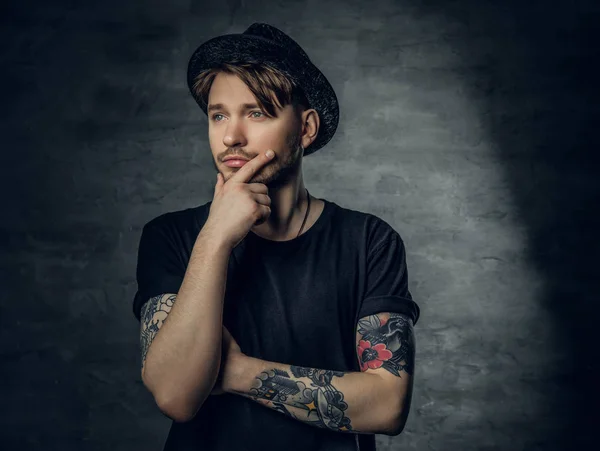 Thoughtful male with crossed tattooed arms