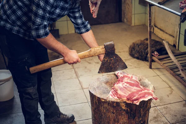 Açougueiro barbudo corta carne com machado — Fotografia de Stock