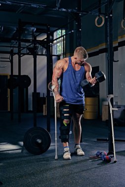 Vücut geliştirmeci koltuk değneği dumbbell tutar.