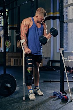 Vücut geliştirmeci koltuk değneği dumbbell tutar.