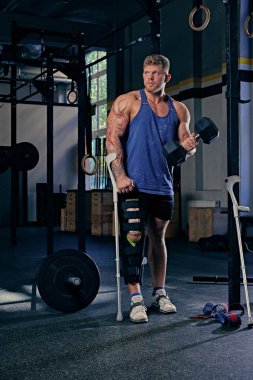 Vücut geliştirmeci koltuk değneği dumbbell tutar.