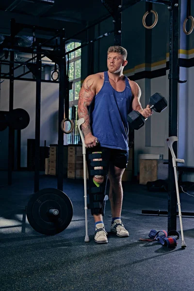 Vücut geliştirmeci koltuk değneği dumbbell tutar.